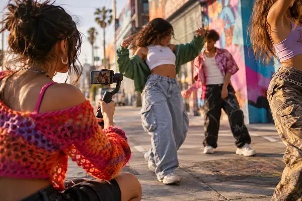 Creator filming colorful street fashion content with friends, spontaneous social media atmosphere.